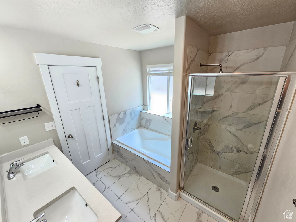 Bathroom featuring marble look tile flooring, a garden tub, a marble finish shower, a textured ceiling, and double vanity