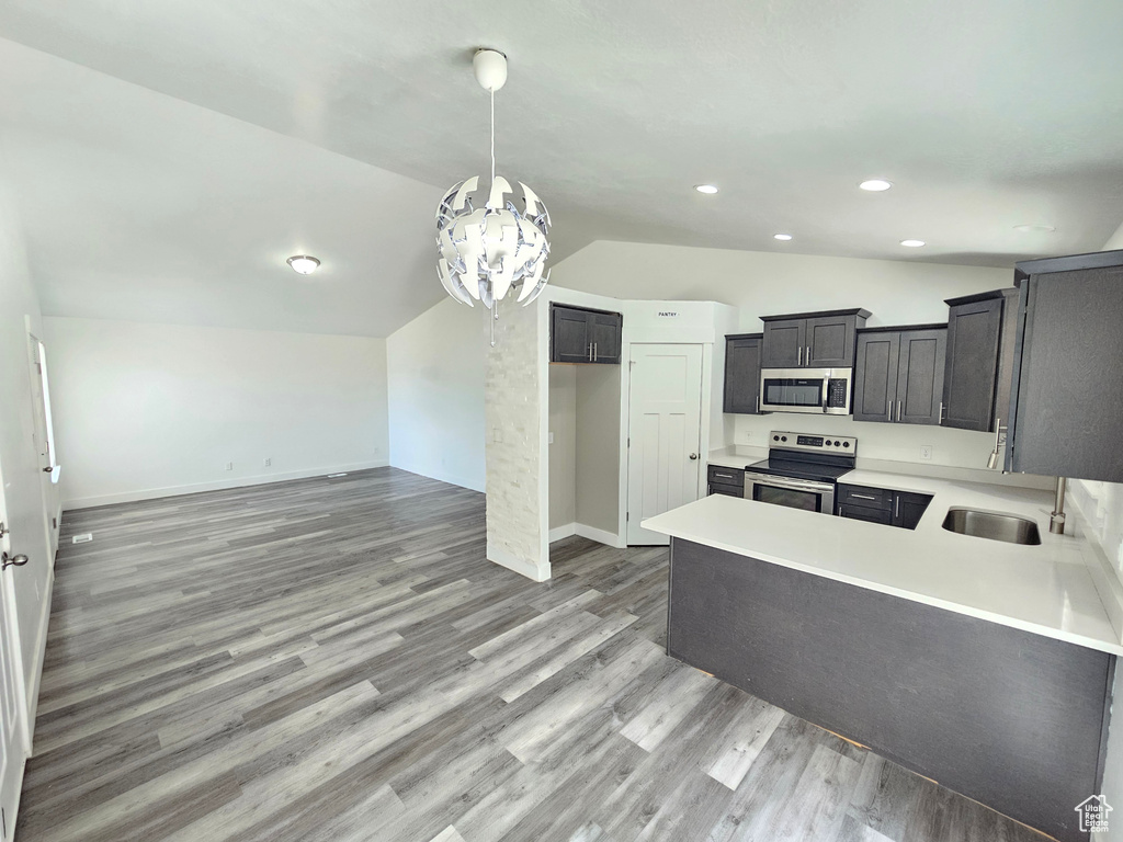 Kitchen with appliances with stainless steel finishes, lofted ceiling, a chandelier, light wood-style flooring, and light countertops