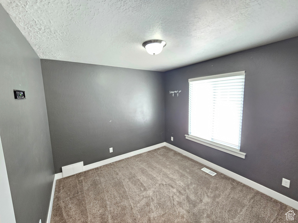 Carpeted spare room featuring a textured ceiling and baseboards