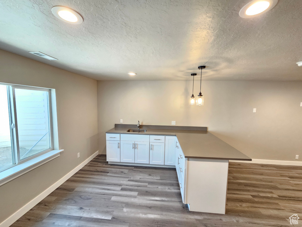 Kitchen featuring a peninsula, wood finished floors, a textured ceiling, recessed lighting, and decorative light fixtures