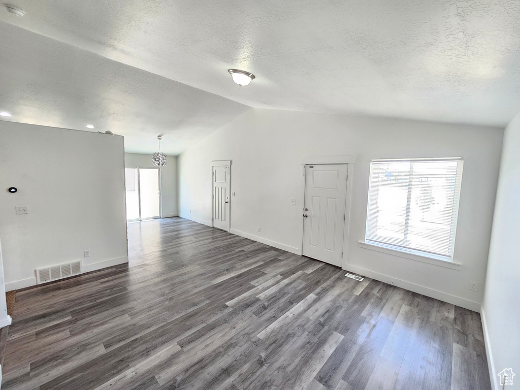 Unfurnished living room with vaulted ceiling, a chandelier, plenty of natural light, dark wood-style flooring, and a textured ceiling