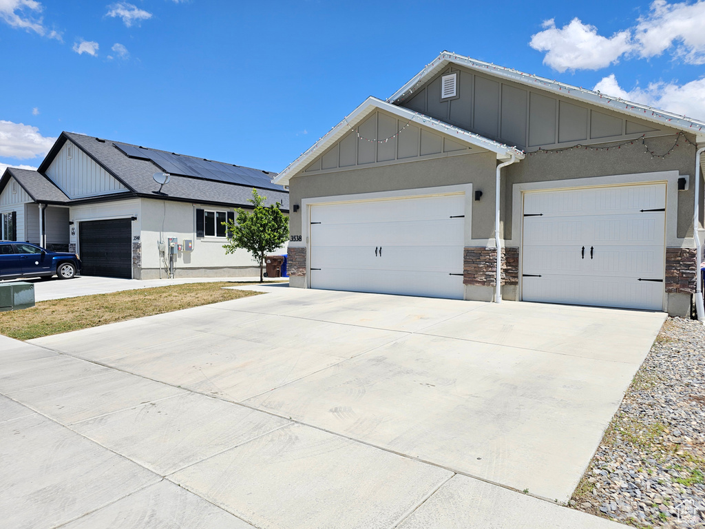 View of front facade featuring stone siding, board and batten siding, a garage, driveway, and stucco siding