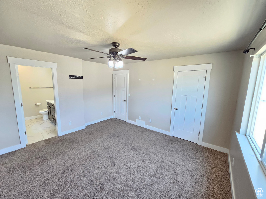 Unfurnished bedroom with light colored carpet, a ceiling fan, ensuite bath, and a textured ceiling