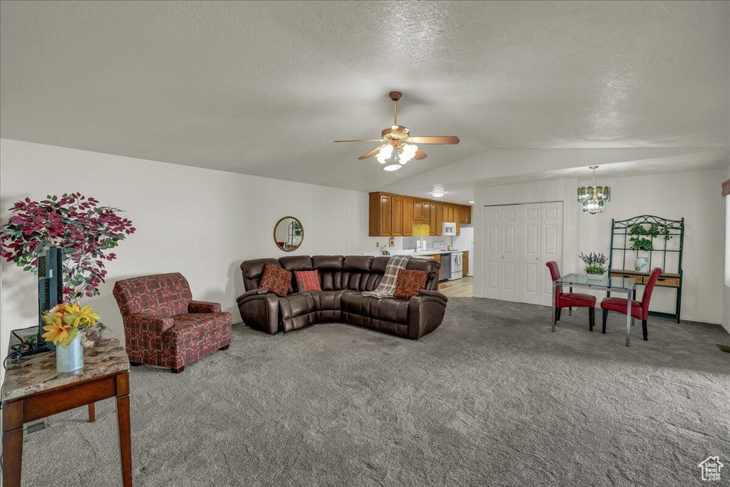 Living room with a chandelier, light colored carpet, vaulted ceiling, ceiling fan, and a textured ceiling