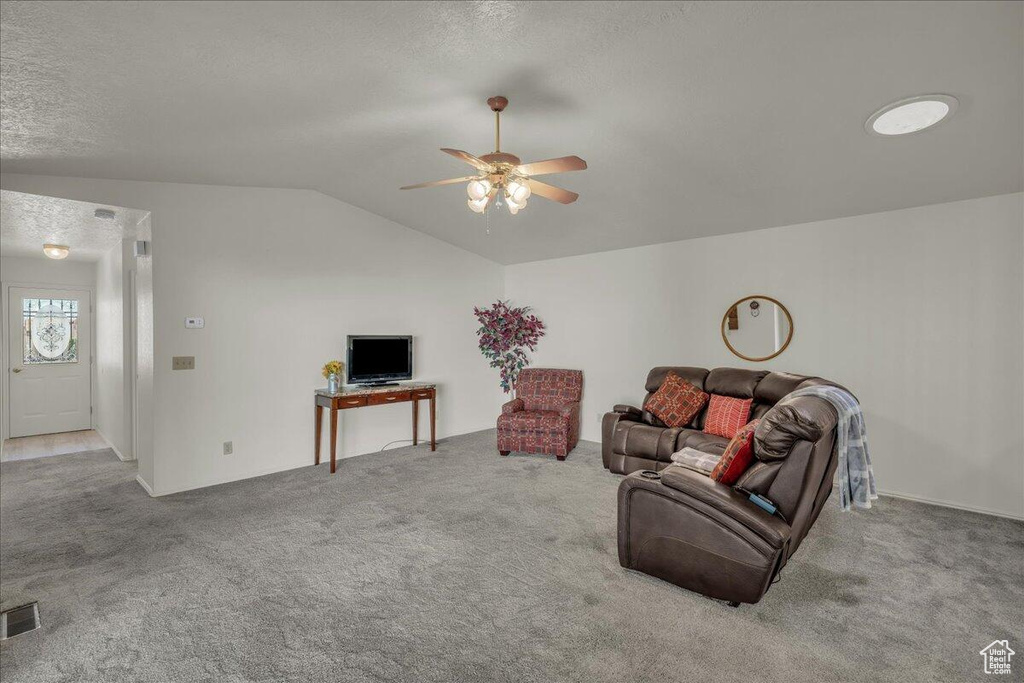 Carpeted living room with lofted ceiling, a ceiling fan, and a textured ceiling