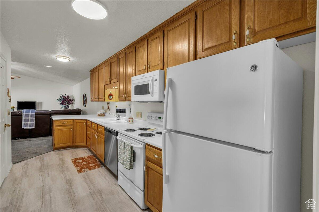 Kitchen featuring white appliances, light wood finished floors, brown cabinetry, vaulted ceiling, and light countertops