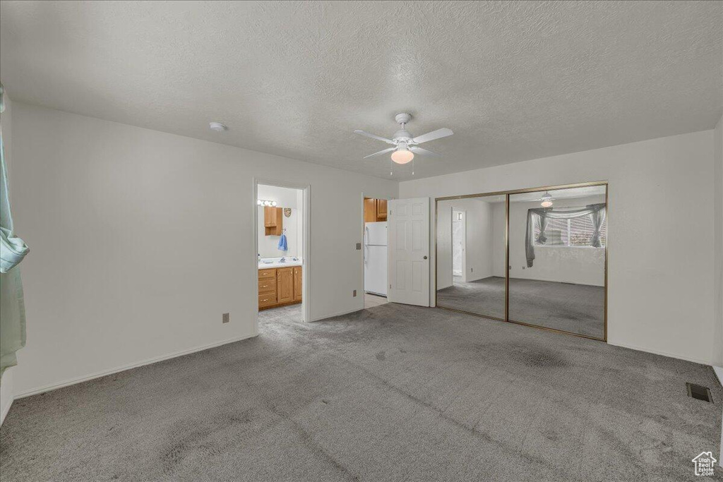 Unfurnished bedroom featuring freestanding refrigerator, carpet flooring, a textured ceiling, a closet, and ceiling fan