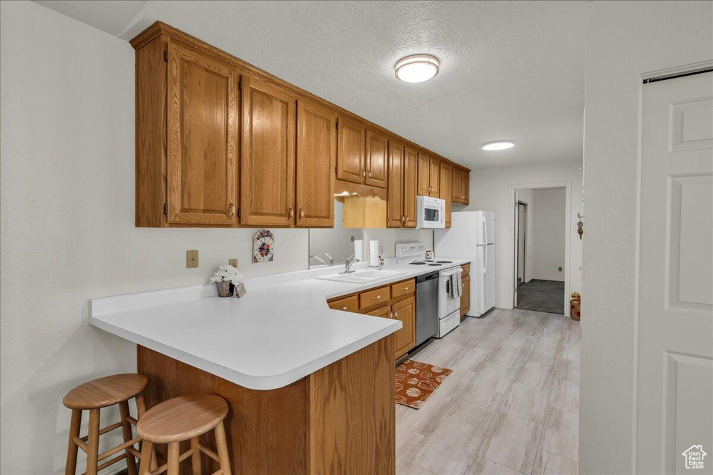 Kitchen featuring white appliances, a breakfast bar, brown cabinetry, light countertops, and a textured ceiling