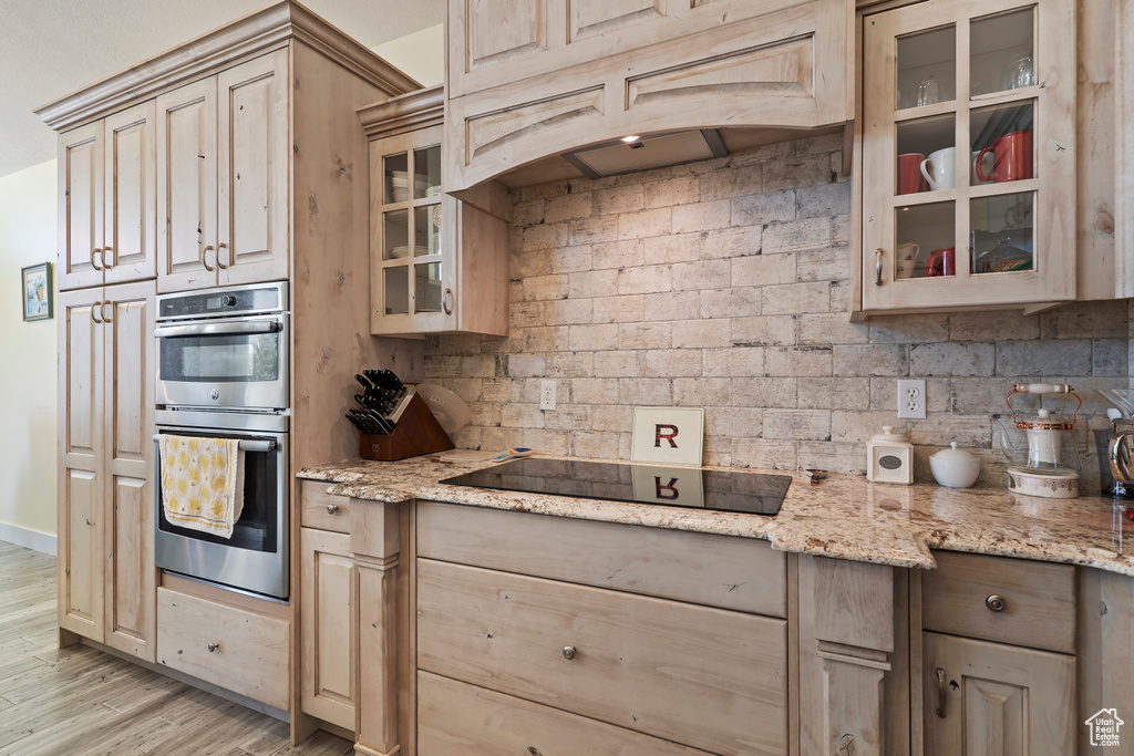 Kitchen featuring black electric cooktop, stainless steel double oven, light wood-type flooring, glass insert cabinets, and tasteful backsplash