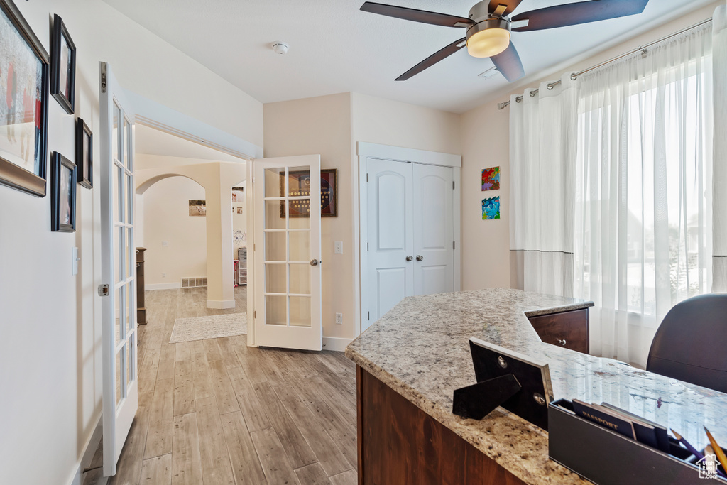 Office space with french doors, arched walkways, light wood-style flooring, and ceiling fan
