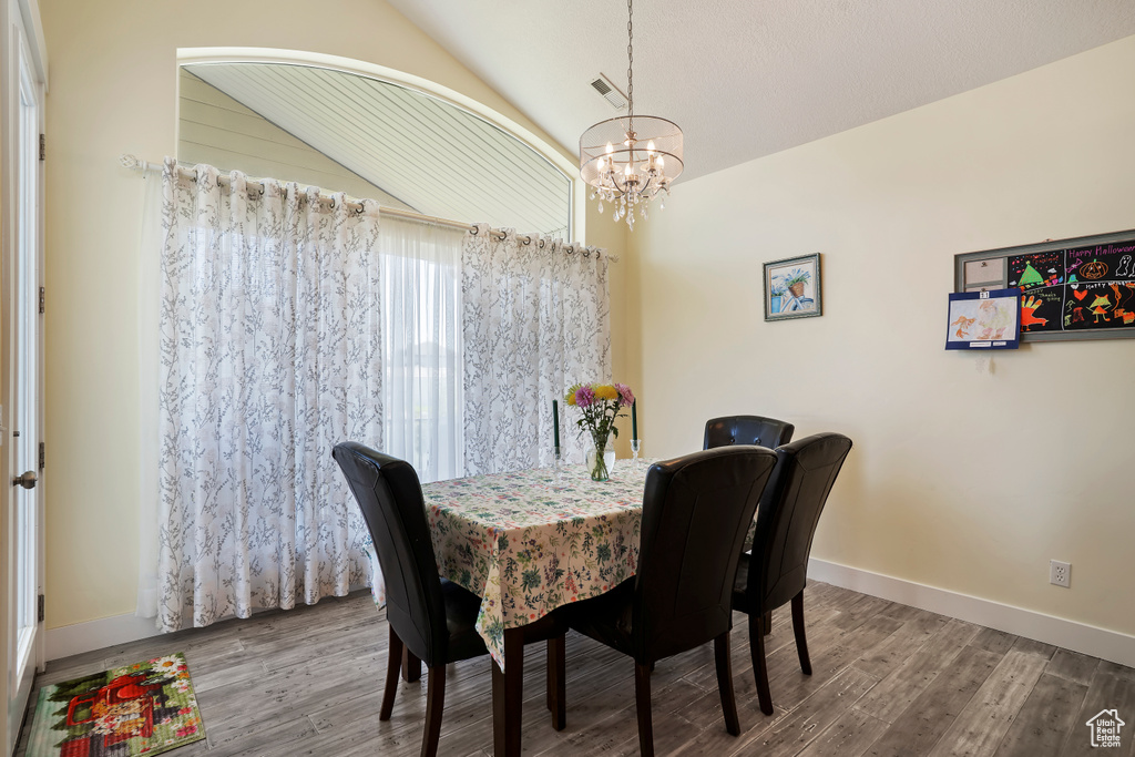 Dining space featuring a chandelier, wood finished floors, and vaulted ceiling