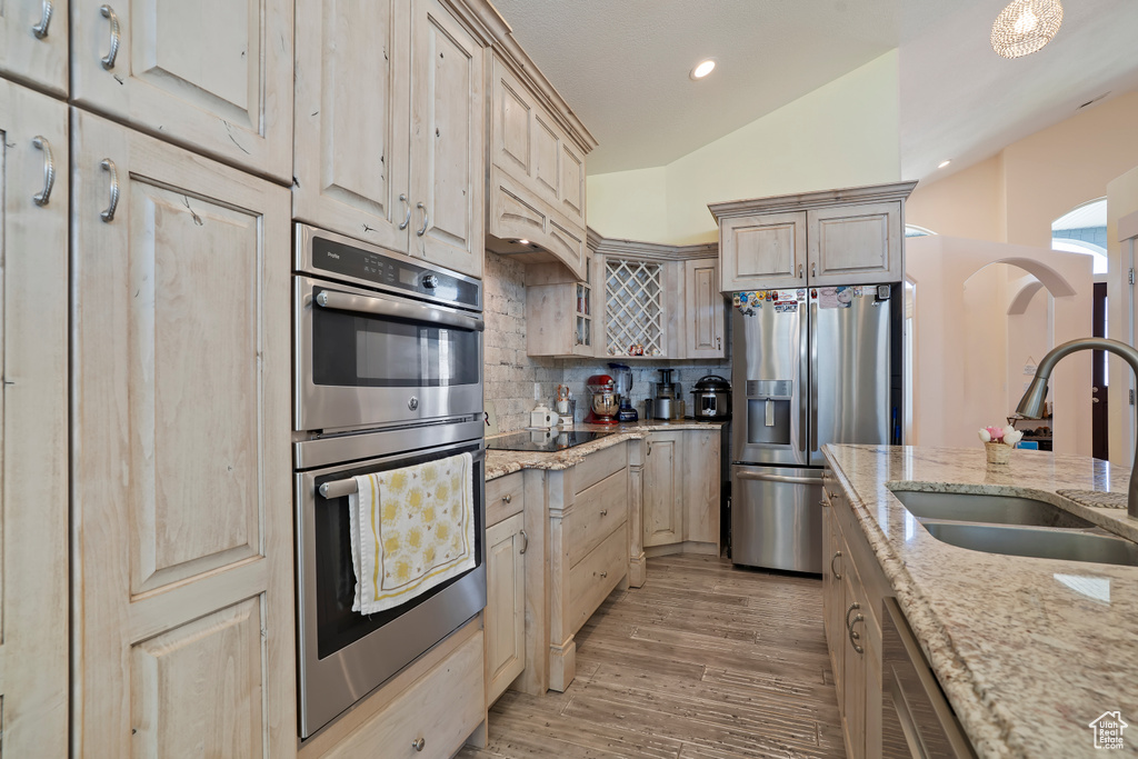 Kitchen with appliances with stainless steel finishes, tasteful backsplash, light stone countertops, light wood-type flooring, and recessed lighting