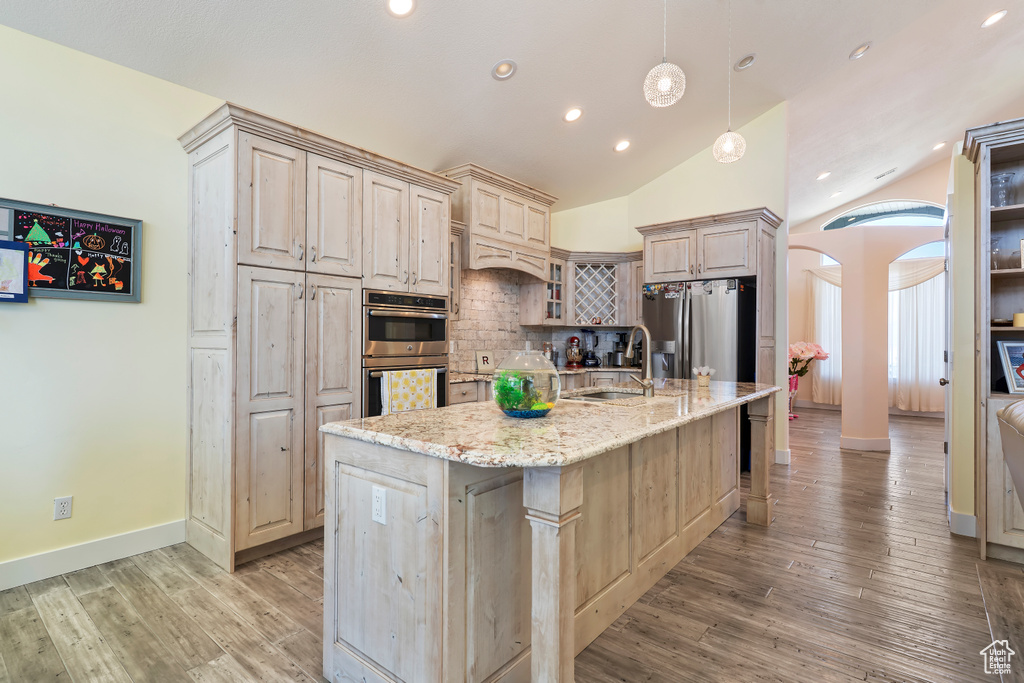 Kitchen with stainless steel appliances, arched walkways, tasteful backsplash, vaulted ceiling, and a spacious island