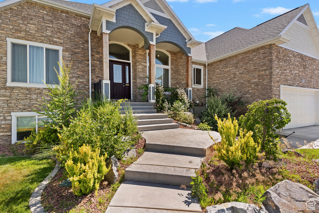 Doorway to property featuring a garage, stone siding, a shingled roof, and covered porch