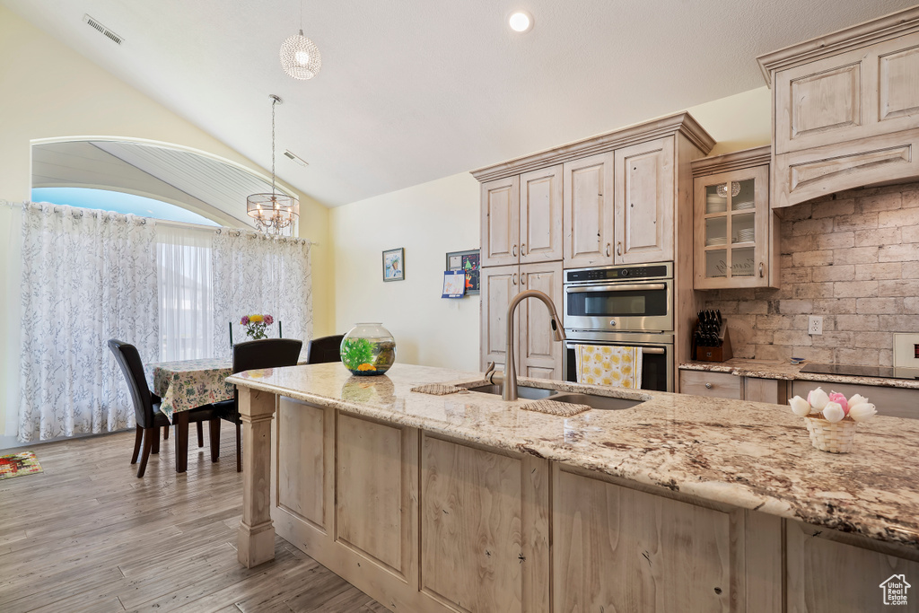 Kitchen with double oven, light stone counters, lofted ceiling, light brown cabinetry, and black electric stovetop