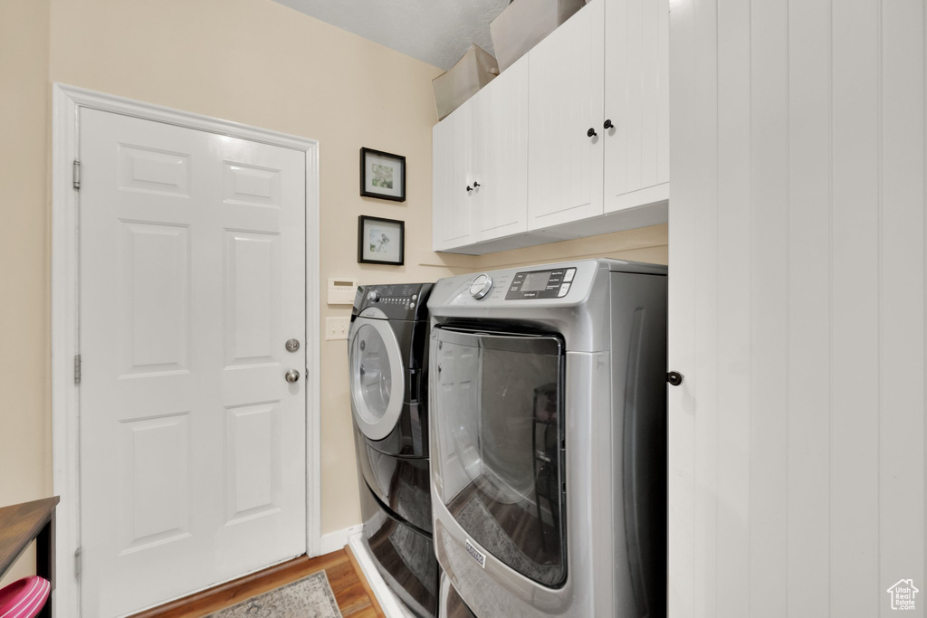 Washroom with washing machine and clothes dryer, light wood-style floors, and cabinet space