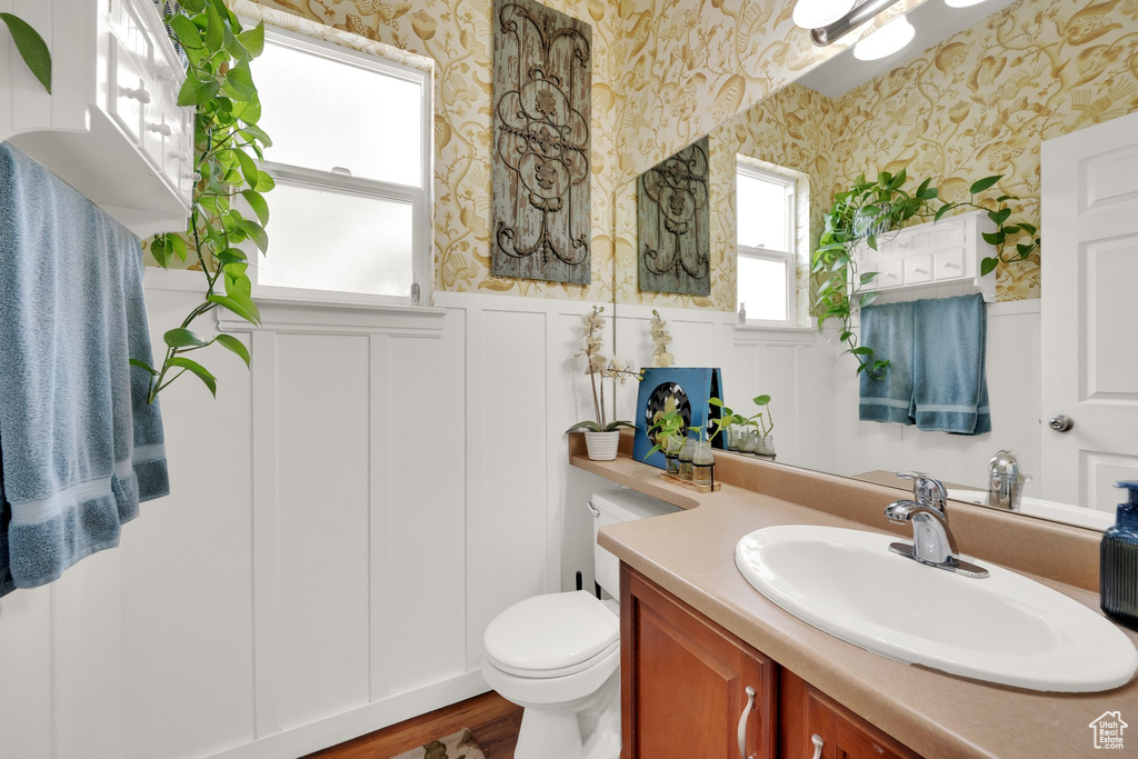 Bathroom with wallpapered walls, a wainscoted wall, vanity, and wood finished floors