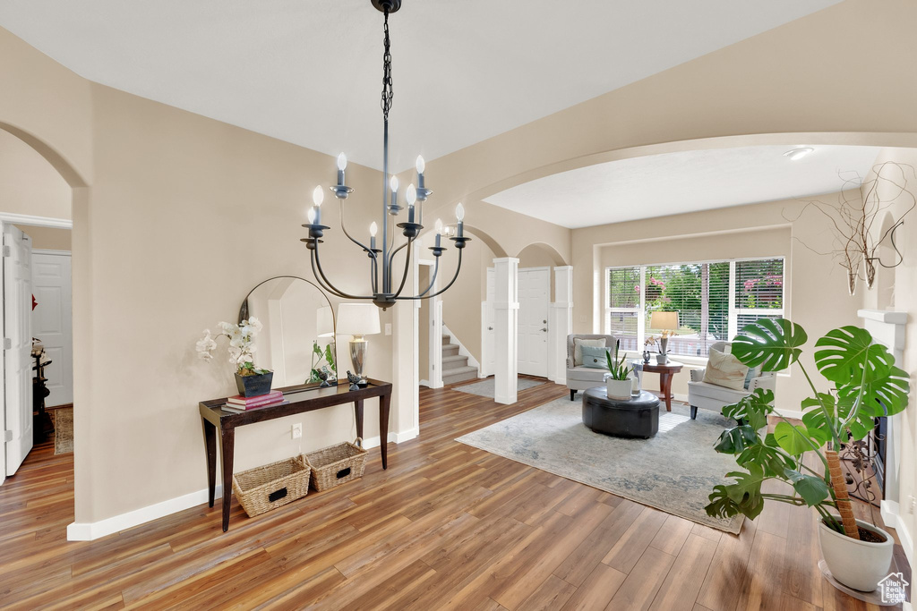 Living area with arched walkways, light wood-style floors, a chandelier, and stairs