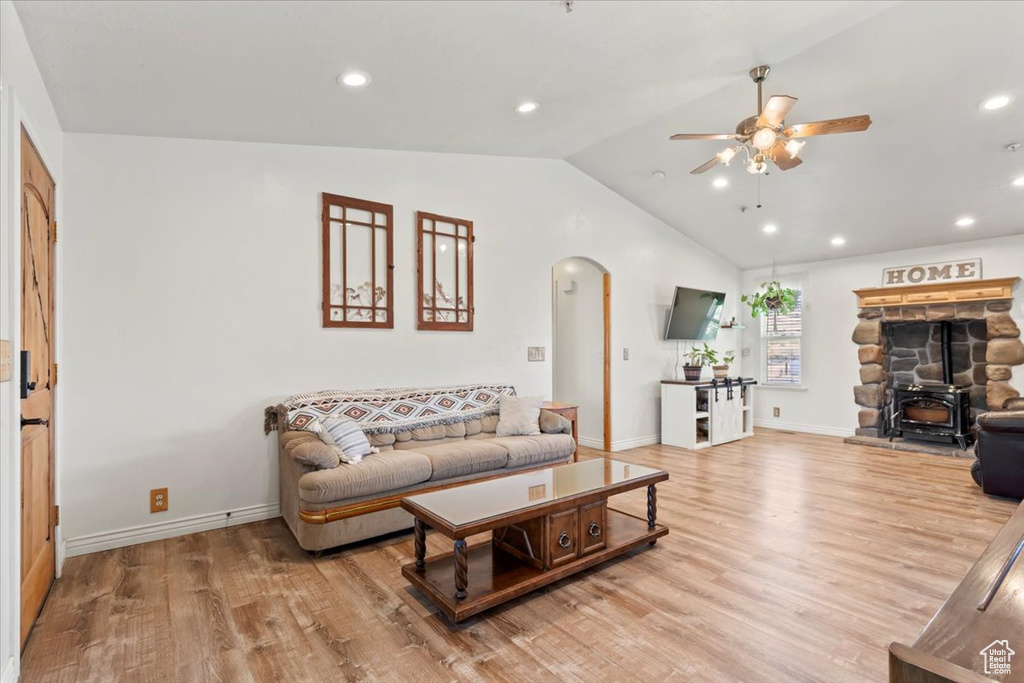 Living room with arched walkways, ceiling fan, lofted ceiling, a wood stove, and light wood-type flooring