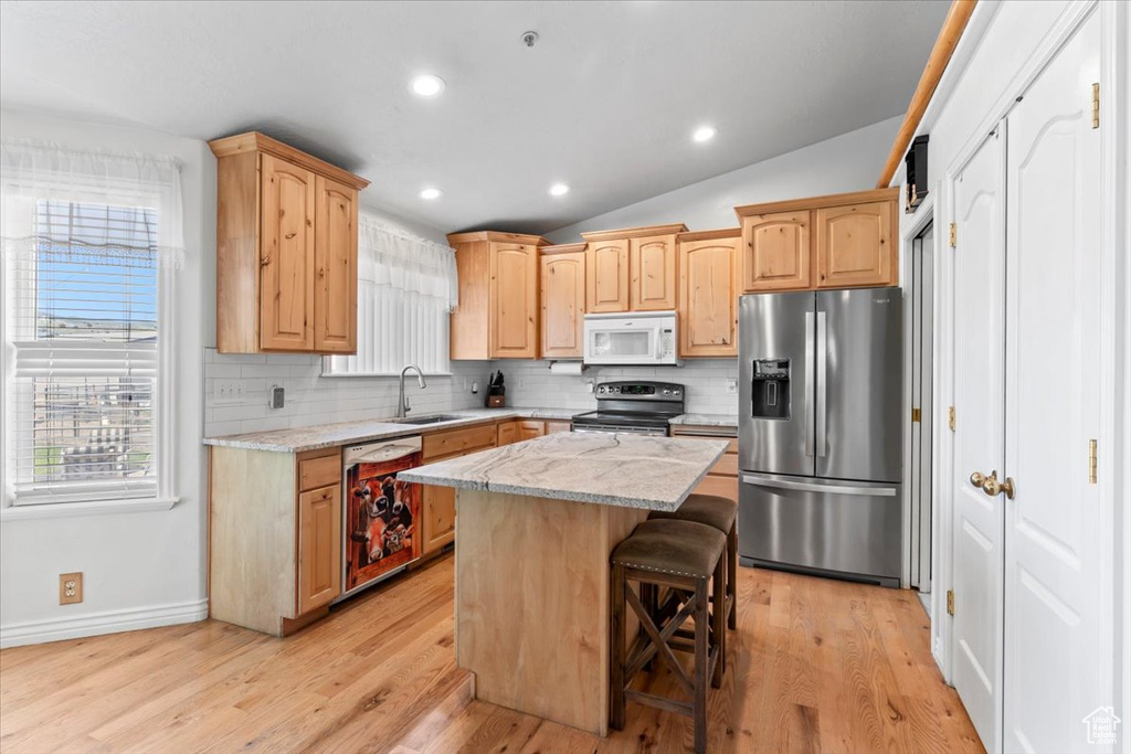 Kitchen with stainless steel appliances, backsplash, light wood-type flooring, light brown cabinets, and a center island
