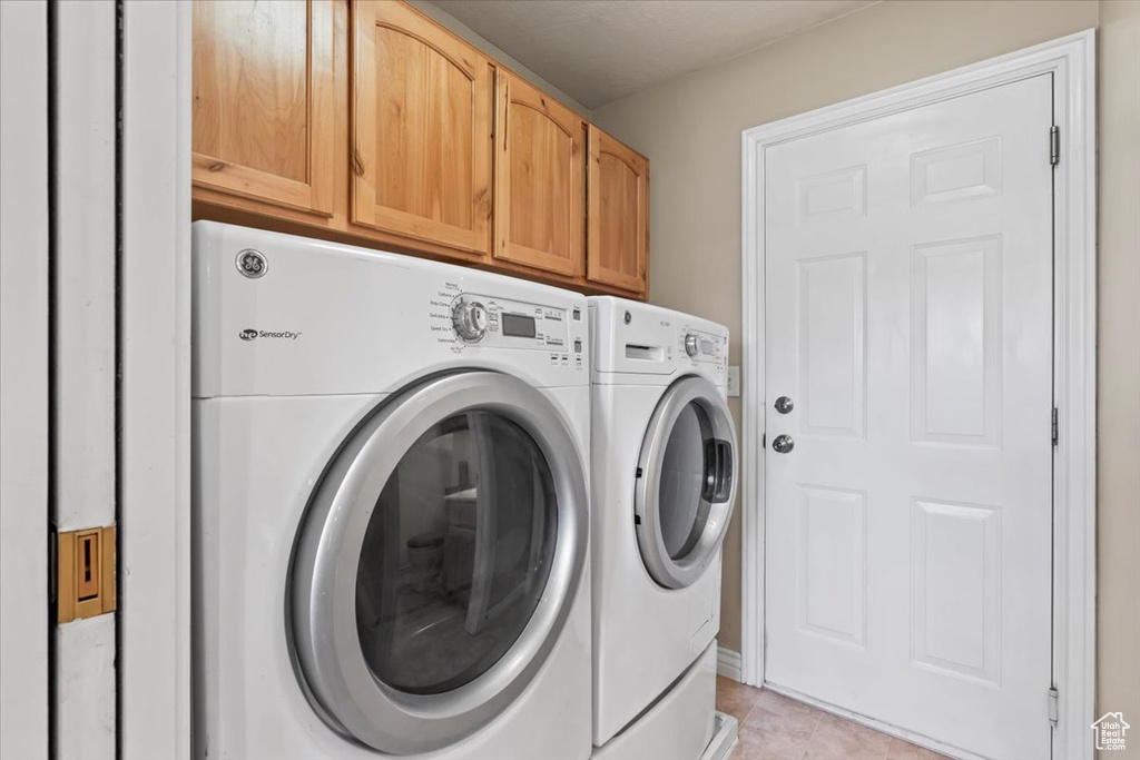 Laundry room featuring washing machine and clothes dryer, cabinet space, and light tile patterned floors