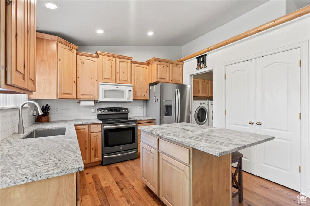 Kitchen featuring appliances with stainless steel finishes, lofted ceiling, independent washer and dryer, light brown cabinets, and a kitchen breakfast bar