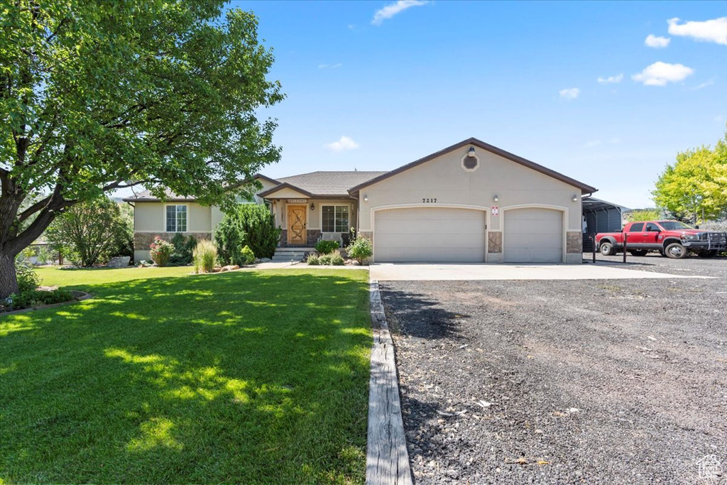 Single story home featuring stone siding, gravel driveway, a garage, a front lawn, and stucco siding
