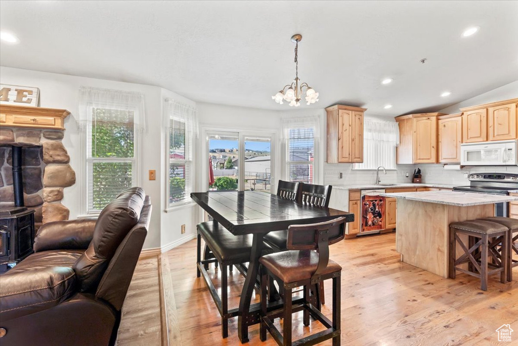 Dining room with light wood finished floors, a chandelier, recessed lighting, and a wood stove