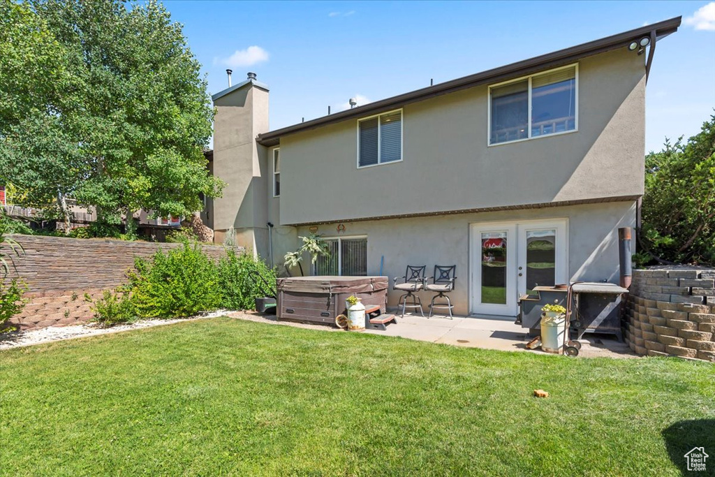 Back of house with a hot tub, french doors, a patio area, stucco siding, and a lawn