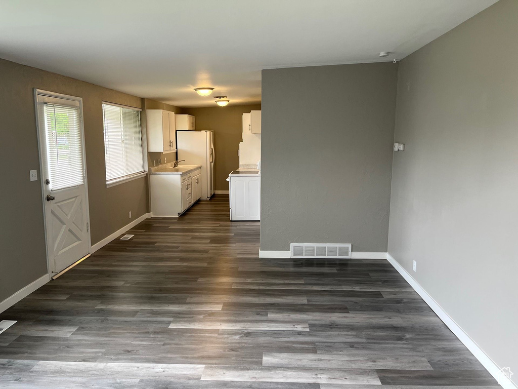 Unfurnished living room featuring dark wood-style flooring and baseboards
