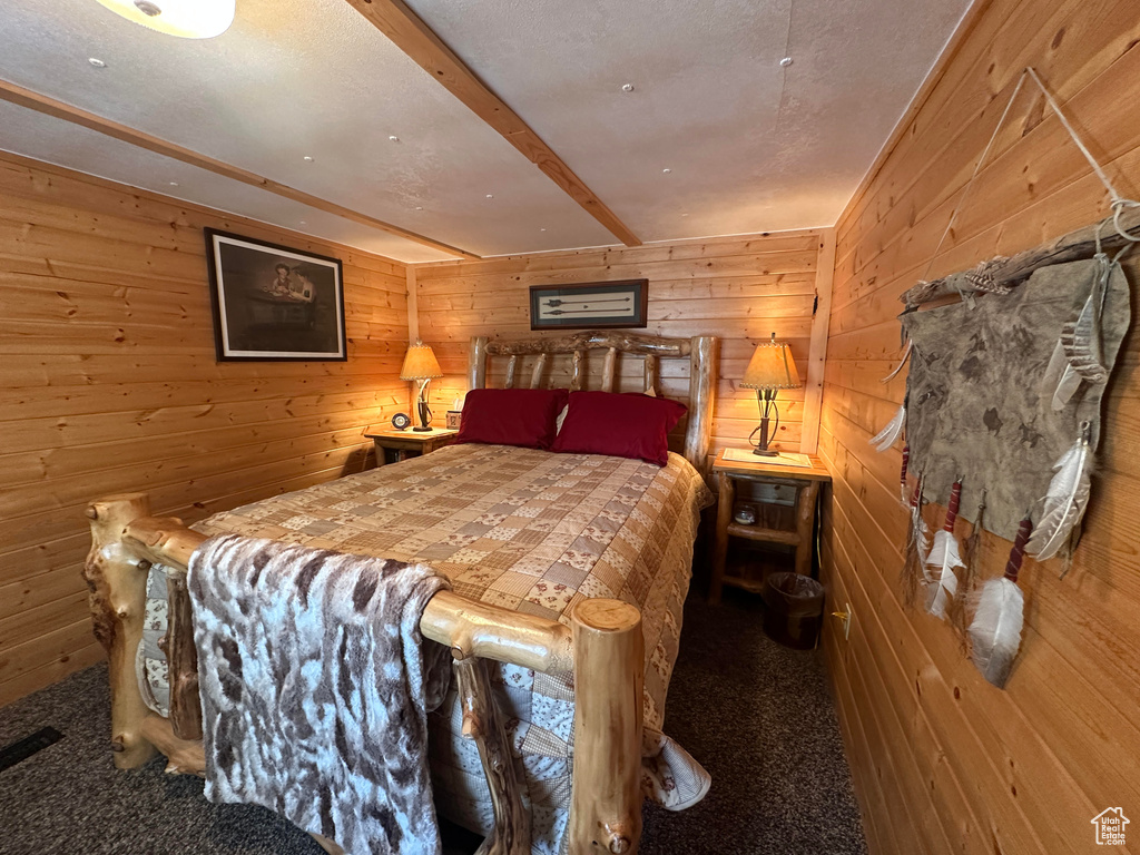 Carpeted bedroom with wood walls and beamed ceiling
