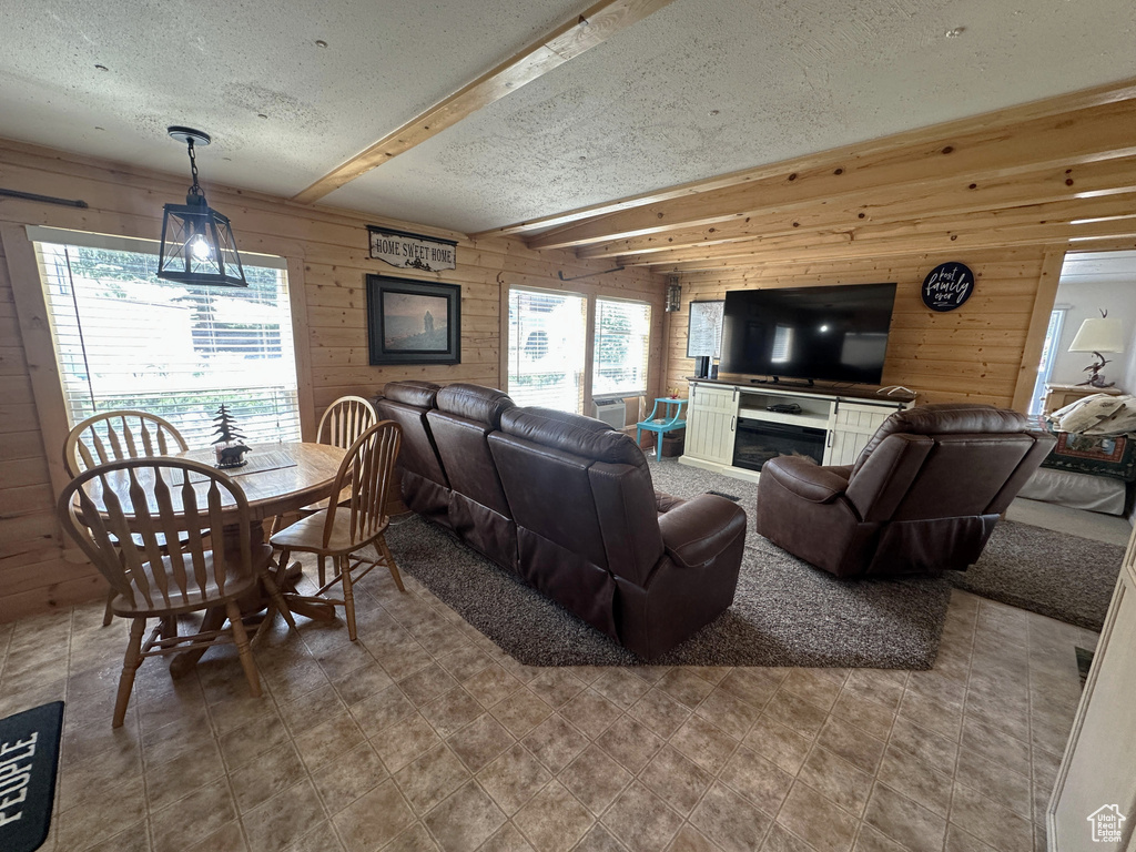 Living room with a textured ceiling, wood walls, beam ceiling, and tile patterned floors