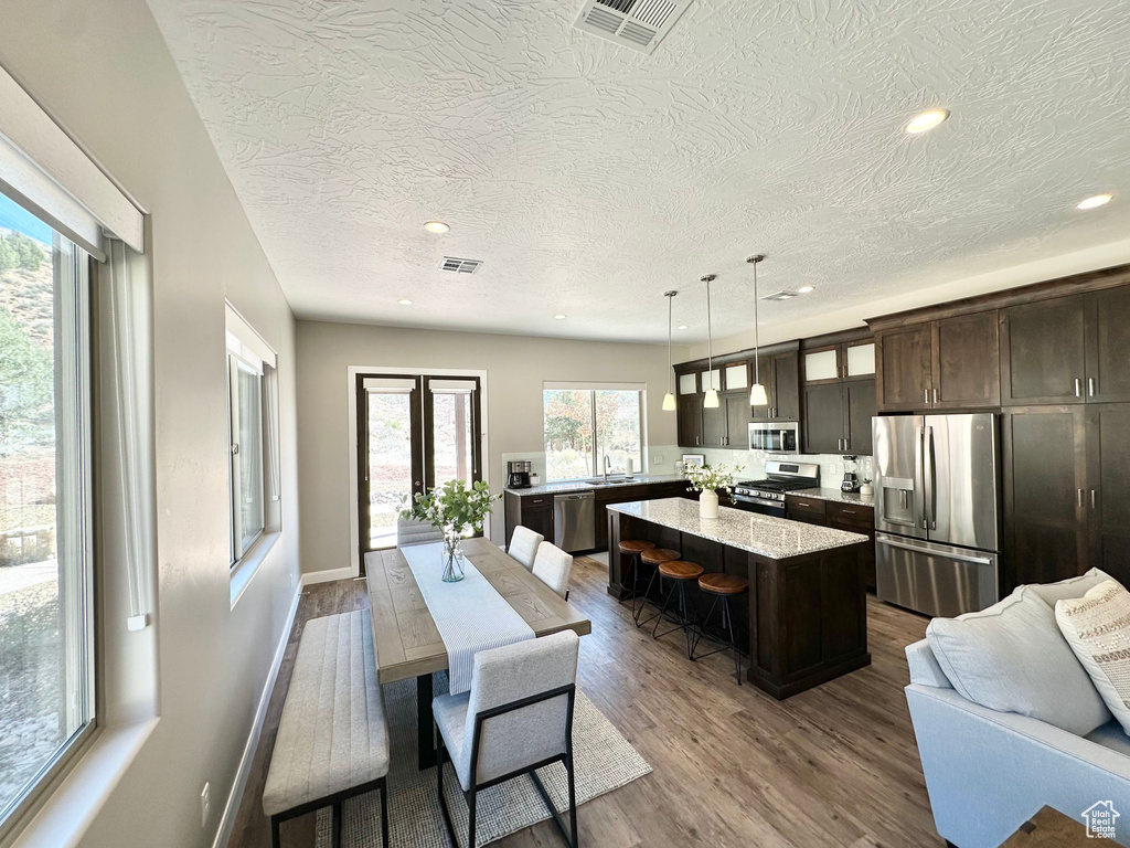 Kitchen with appliances with stainless steel finishes, a textured ceiling, recessed lighting, dark brown cabinets, and dark wood finished floors
