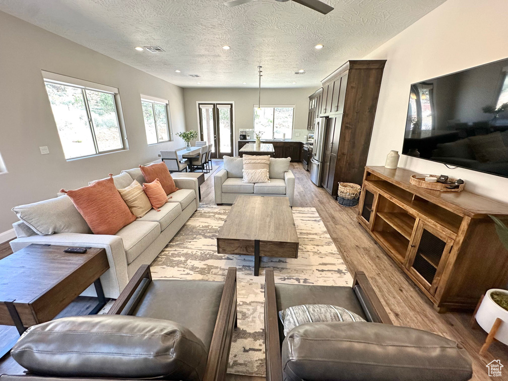 Living area with light wood-type flooring, a textured ceiling, ceiling fan, and recessed lighting