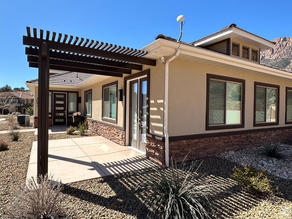 Back of property with stone siding, stucco siding, a pergola, and a patio area