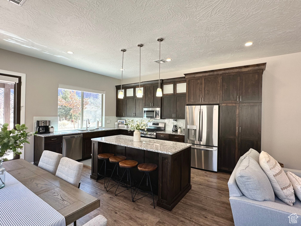 Kitchen featuring appliances with stainless steel finishes, dark brown cabinets, decorative backsplash, open floor plan, and dark wood finished floors