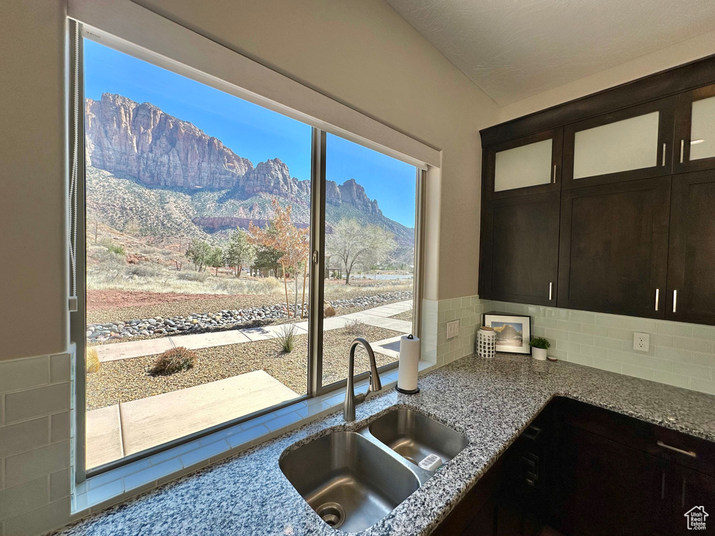 Kitchen featuring light stone counters, glass insert cabinets, backsplash, a mountain view, and dark brown cabinetry