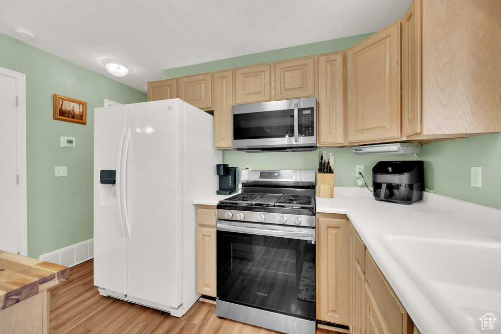 Kitchen with stainless steel appliances, light brown cabinets, light countertops, and light wood-style floors