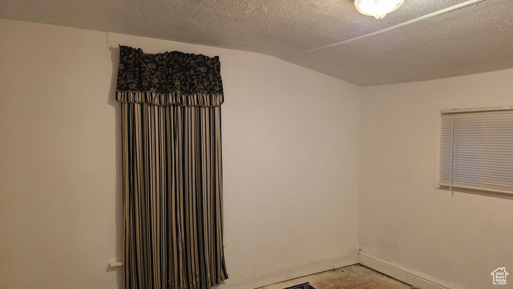 Empty room featuring vaulted ceiling and a textured ceiling