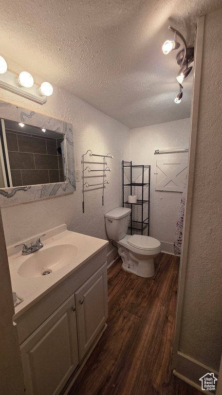 Full bath with wood finished floors, a textured ceiling, vanity, and a textured wall