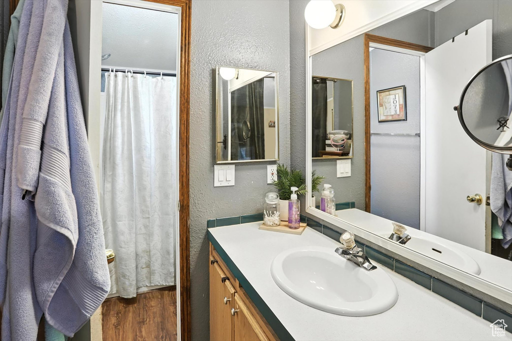 Full bathroom with a textured wall, wood finished floors, and vanity