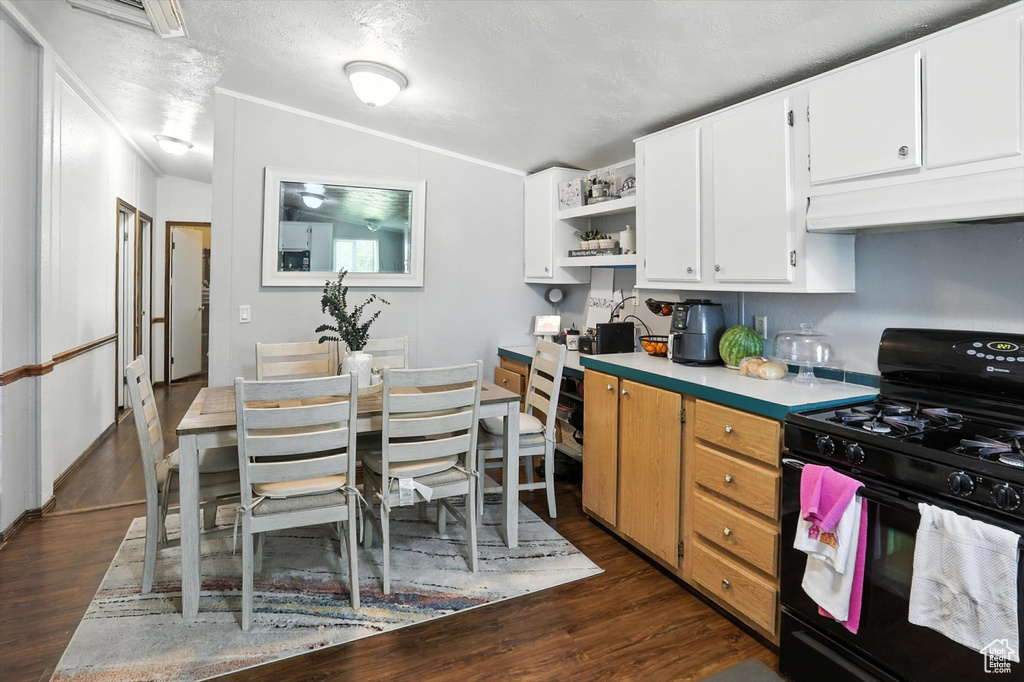 Kitchen with black range with gas stovetop, under cabinet range hood, open shelves, dark wood-style floors, and white cabinets