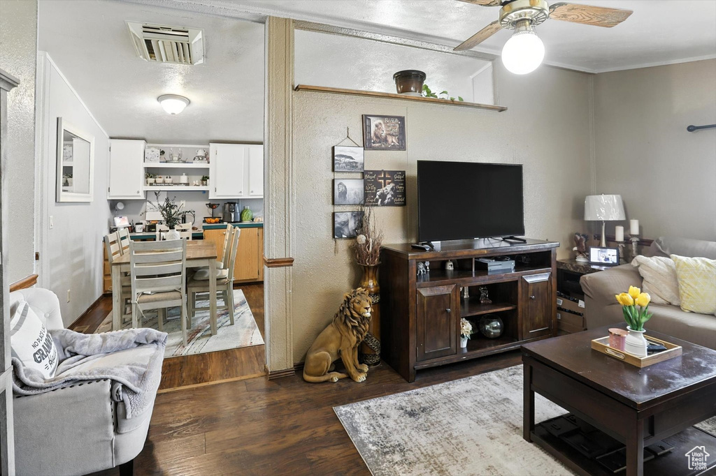 Living room with dark wood-type flooring, ceiling fan, and crown molding