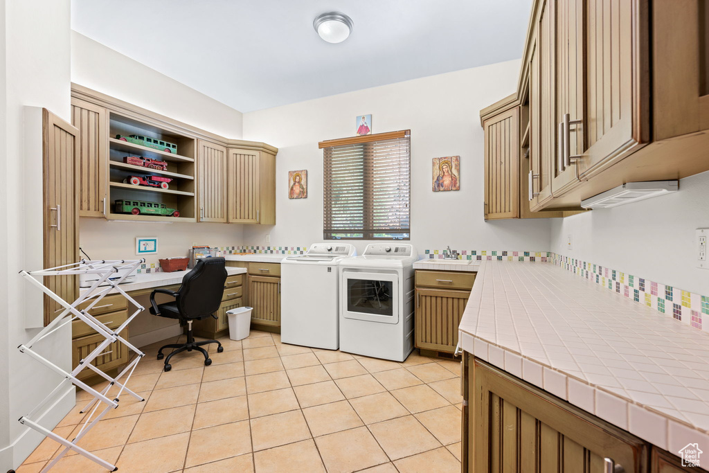 Laundry area with cabinet space, washer and clothes dryer, light tile patterned floors, and a desk