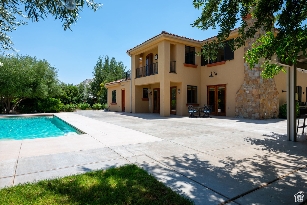 Back of property featuring stucco siding, a patio, a balcony, an outdoor pool, and a tiled roof