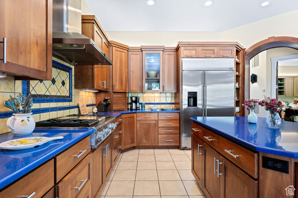 Kitchen with extractor fan, appliances with stainless steel finishes, dark countertops, decorative backsplash, and brown cabinetry