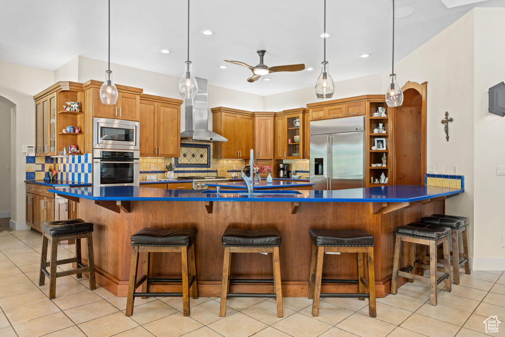 Kitchen featuring built in appliances, open shelves, wall chimney exhaust hood, brown cabinets, and recessed lighting