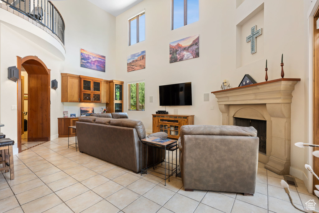 Living room with a fireplace with raised hearth, a towering ceiling, arched walkways, and light tile patterned flooring