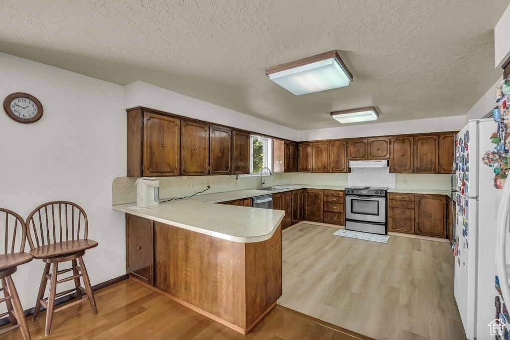 Kitchen with stainless steel appliances, under cabinet range hood, a peninsula, light wood-style floors, and a textured ceiling