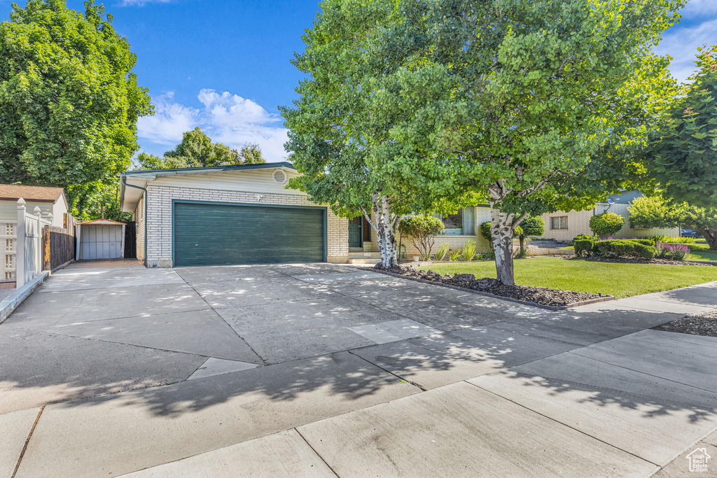 View of property hidden behind natural elements featuring a garage, concrete driveway, brick siding, and a gate